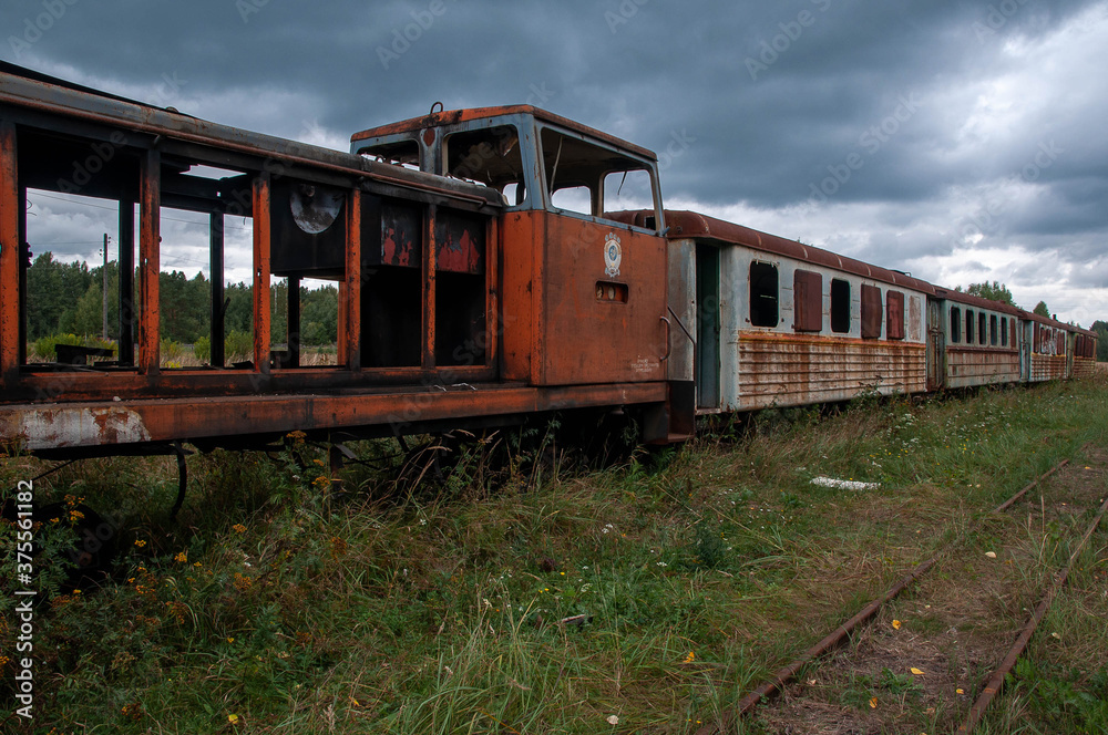 Old rusty diesel locomotive with broken passenger cars on the railway