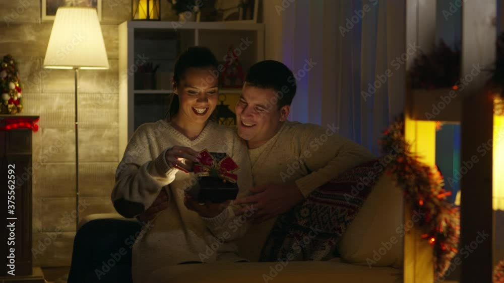 Excited young woman receives a gift with magical shine from her husband on christmas day. Receiving Xmas surprise from loved one. Giving happy romantic present gift box to significant other in new Excited young woman receives a gift with magical shine from her husband on christmas day. Receiving Xmas surprise from loved one. Giving happy romantic present gift box to significant other in new
