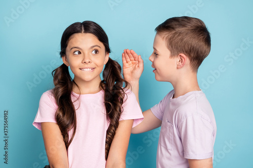 Listen i know where ice cream. Two little people kids boy speak talk private information hand girl bite lips teeth think inspired thoughts wear casual t-shirt isolated blue color background photo