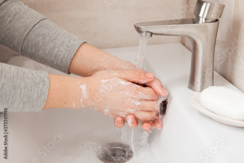 Women's hands close-up under running water in the bathroom above the sink. There's a piece of soap nearby