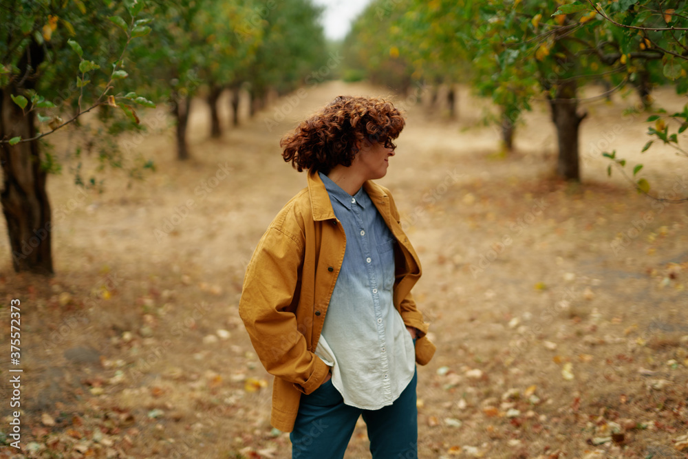 Young caucasian curly woman in jeans shirt and orange jacket relaxing in the autumn park on a sunny day. Fall and autumn concept. Young caucasian curly woman in jeans shirt and orange jacket relaxing in the autumn park on a sunny day. Fall and autumn concept.