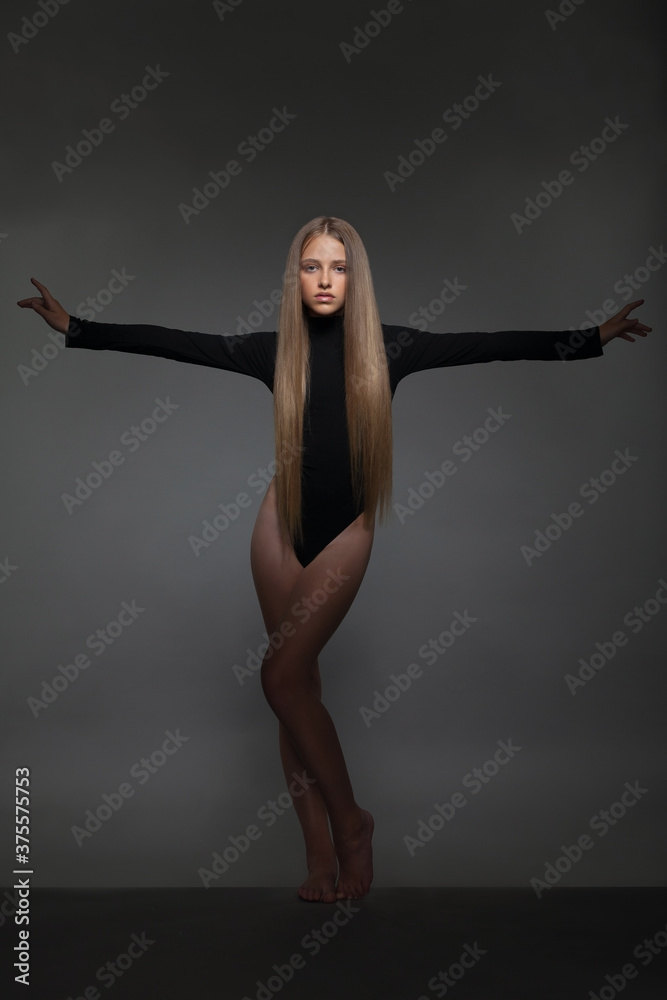 Beautiful girl teenager blonde in a black bodysuit in the studio
