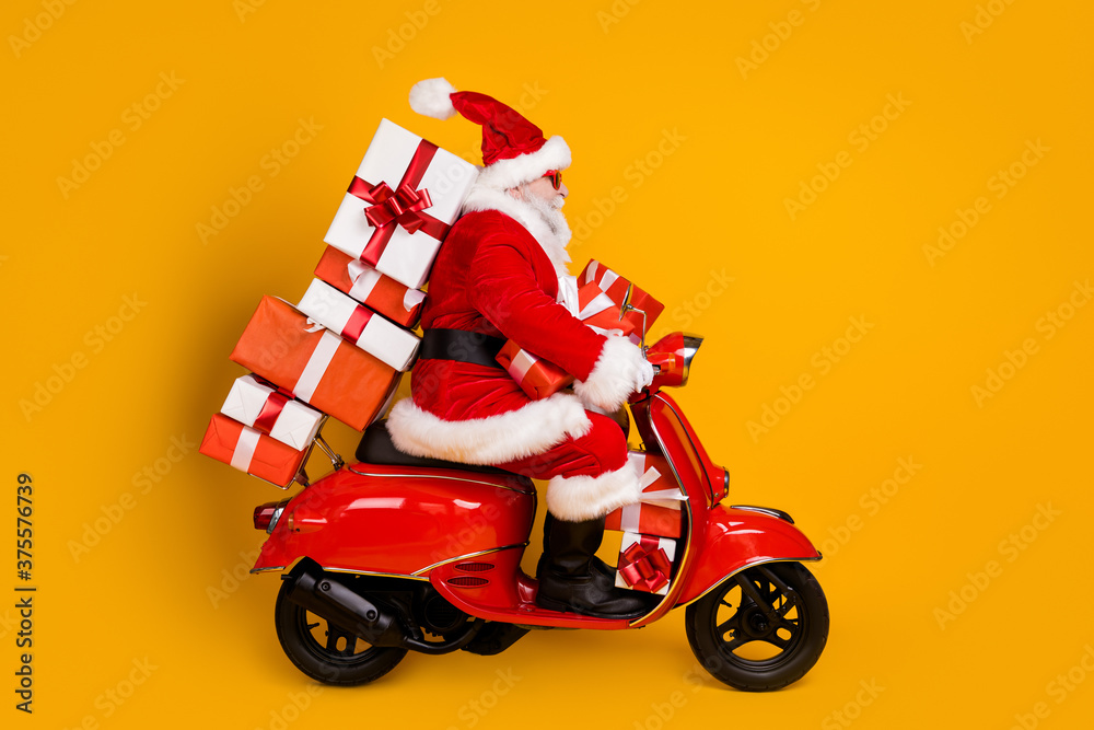 Profile side view of his he nice funny white-haired Santa St Nicholas  riding moped hurry up rush carrying bringing pile stack gifts December  isolated bright vivid shine vibrant yellow color background Stock