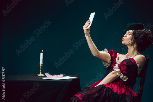 Selfie mood. Young woman as Anna Karenina isolated on dark blue background. Retro style, comparison of eras concept. Beautiful female model like literature character, great, old-fashioned. photo