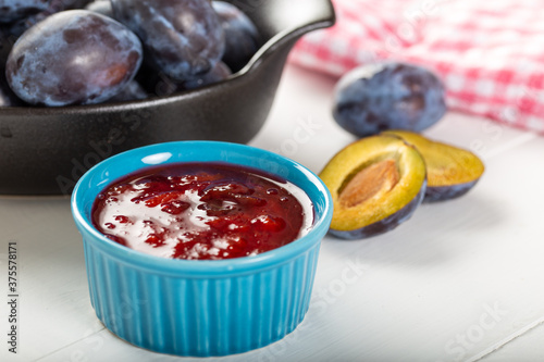 Homemade damson plum jam in blue ceramic bowl and berries on white wooden background.