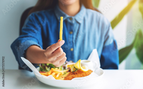 Closeup image of a woman holding a piece of french fries and fish and chips on table in the restaurant