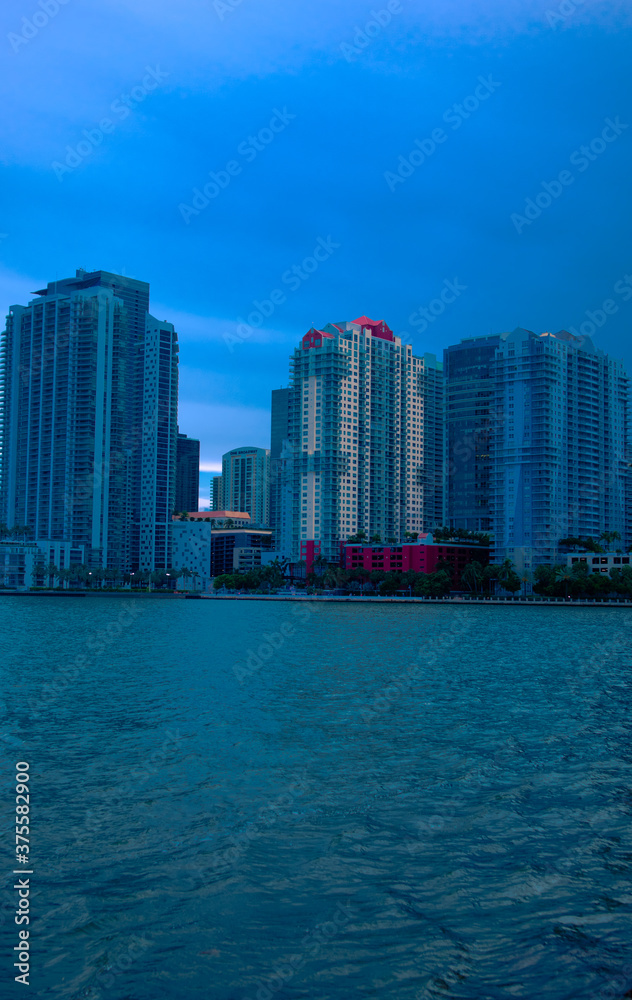 Naklejka premium View of buildings in Brickell Miami, Florida as night time nears, High rises near water in Miami, Cold look of buildings, Cold look of high rises, Cold look of buildings near water, Nighttime in city
