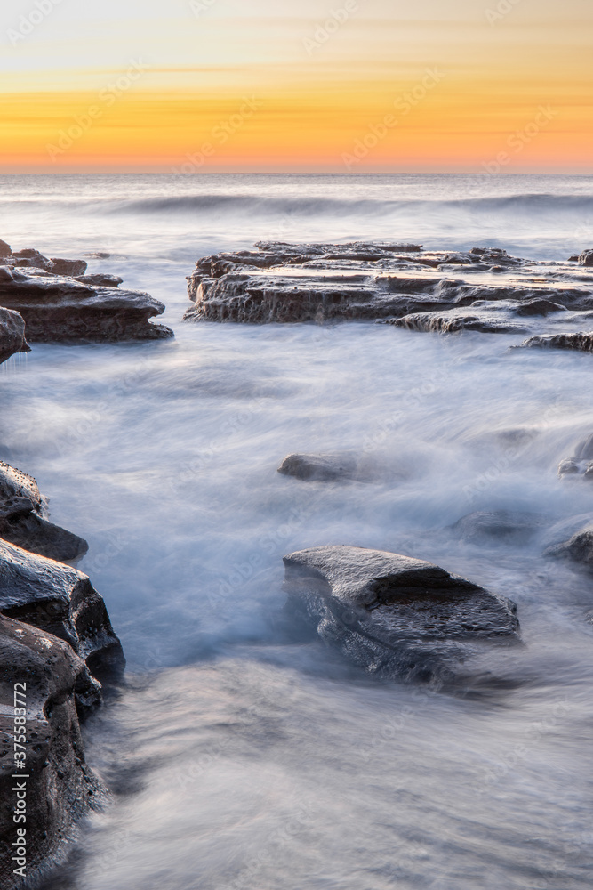 Obraz premium Ocean water flow between rocks during dawn at Coalcliff Beach, Australia.