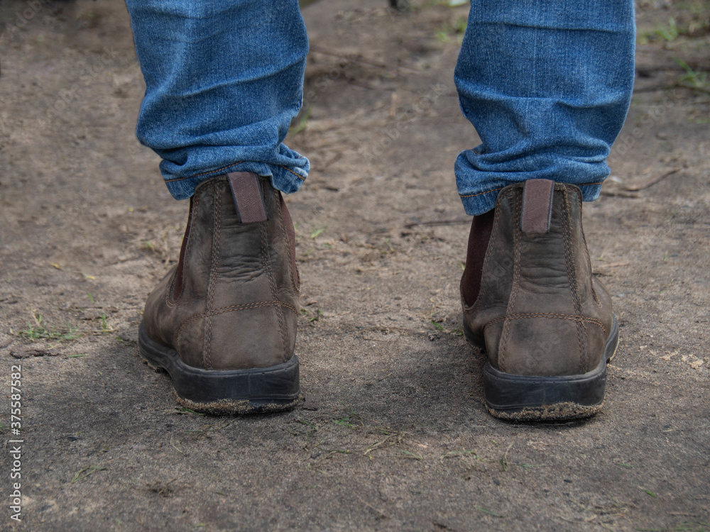 Legs of man standing on wet ground in blue jeans and leather brown shoes