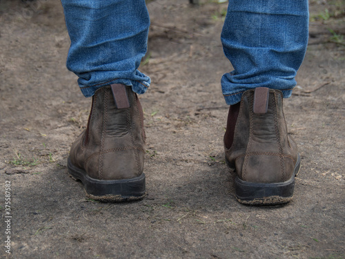Legs of man standing on wet ground in blue jeans and leather brown shoes
