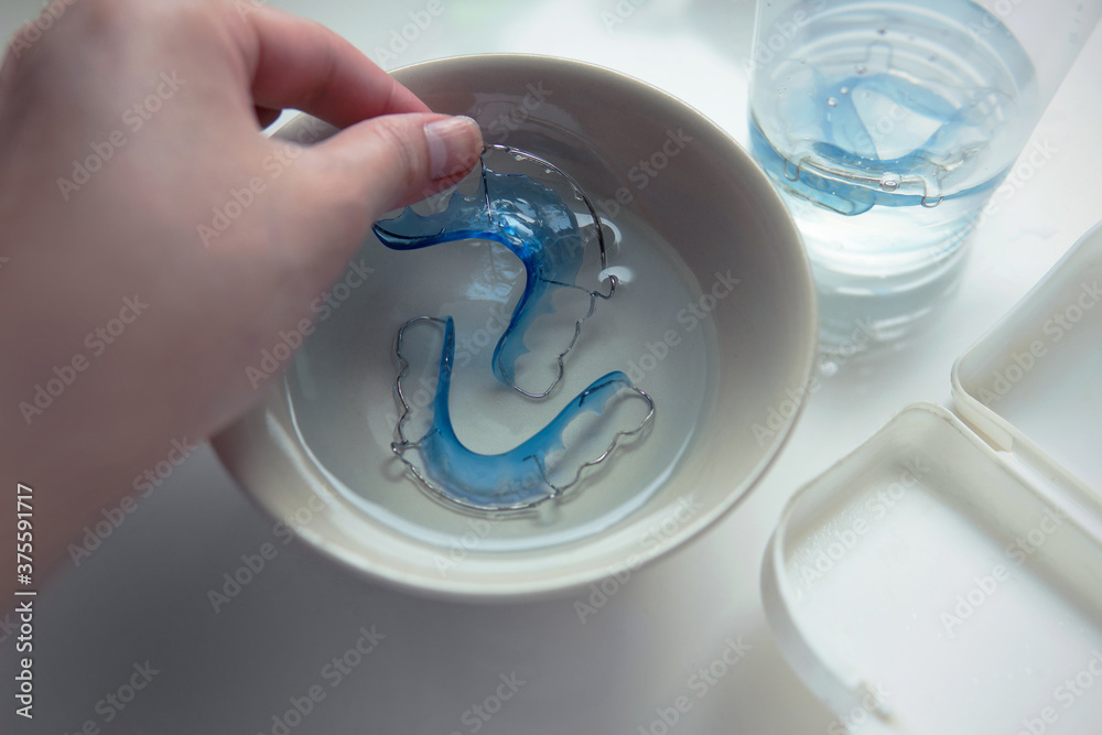 Hand taking blue retainer for cleaning and soaking in a fresh water