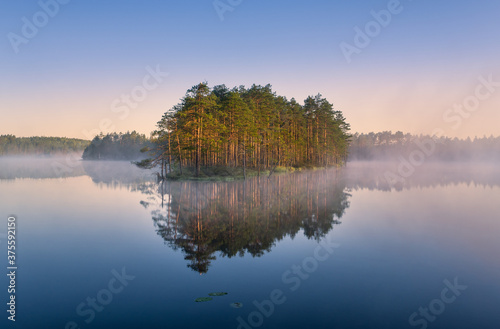 Scenic nature landscape with mood fog and beautiful sunrise at early summer morning in lakeside Finland