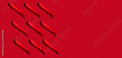 Pattern of nine red hot chili peppers in hard light against red background. Copy space.