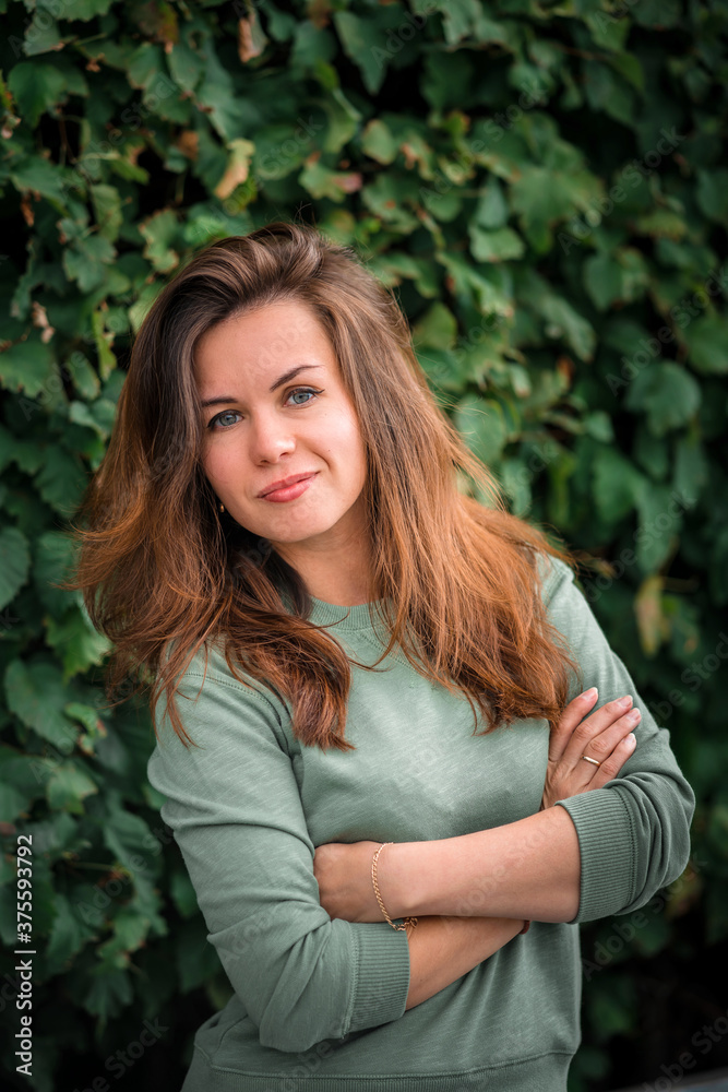 Portrait of a young brunette woman with long hair on a background of green leaves Portrait of a young brunette woman with long hair on a background of green leaves