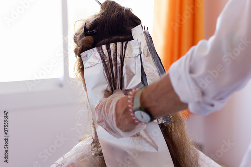 Fotografija Hair stylist with plastic gloves doing streaks to customer hair at home
