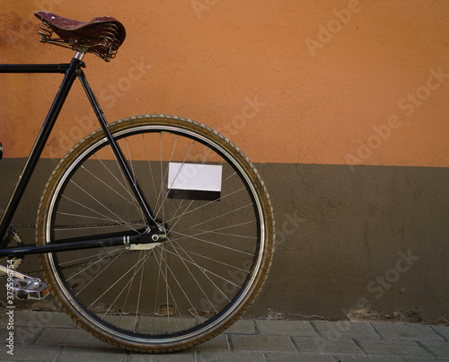 stylish old style black  bicycle on brown and orange wall background.  bicycle parked  exterior. cement  wall background. empty postcard between spokes