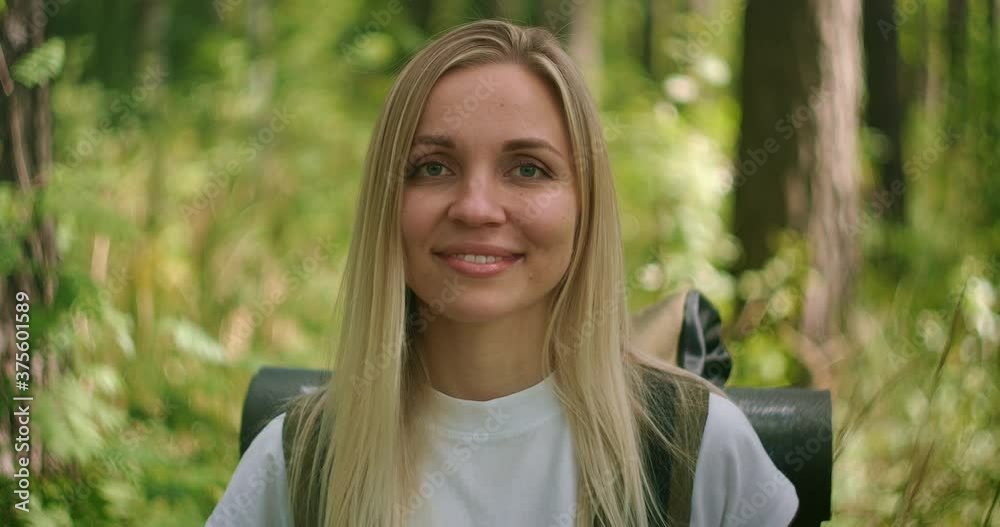 Portrait of a young woman traveler in the sun looking directly into the camera and smiling flirting, Traveler with a backpack in the Park and in the woods in slow motion Portrait of a young woman traveler in the sun looking directly into the camera and smiling flirting, Traveler with a backpack in the Park and in the woods in slow motion