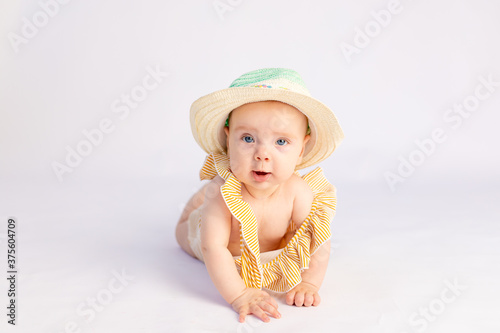 smiling baby girl 6 months old in a swimsuit and sun hat lying on a white isolated background, space for text