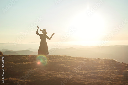 silhouette of a woman with arms outstretched in sunset light in mountains