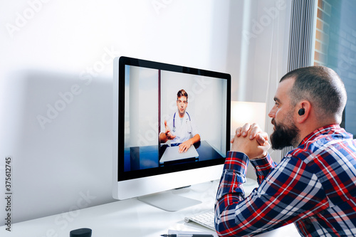 Young man in front of computer having virtual meeting with his doctor