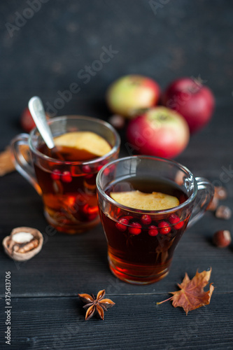 Two cups of autumn warming tea with berries and pieces of apples on a black wooden background. Hot berry tea.