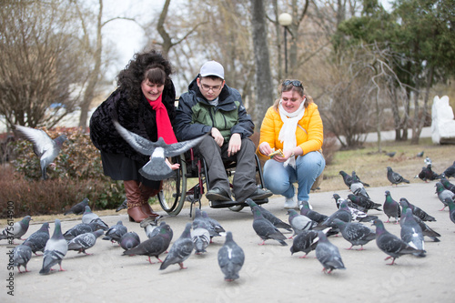 A man in a wheelchair with his family is feeding pigeons © Светлана Лазаренко