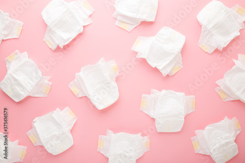 Many white baby diapers on light pink table background. Pastel color. Top down view.