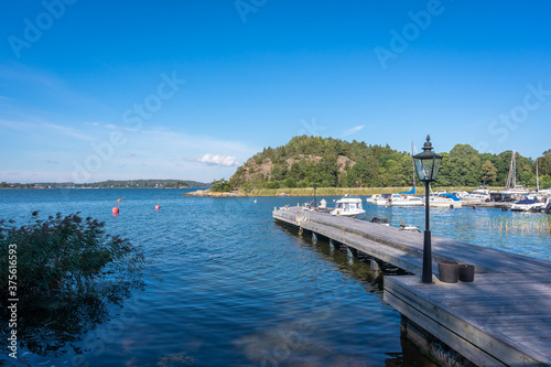 Fototapeta Naklejka Na Ścianę i Meble -  Wooden pier berth Parking for yachts near the residence. A white yacht is moored at its own pier marina on a sunny summer day. Yachting people lifestyle. 