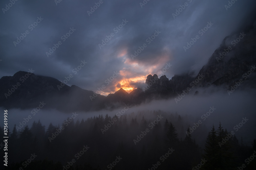 Fototapeta premium Dramatic sunset over Civetta and Moiazza mountain groups on a foggy and cloudy evening as seen from Rifugio Bruto Carestiato, stage 10 of Alta Via 1 trek, Zoldo Dolomites, South Tirol, Italy.