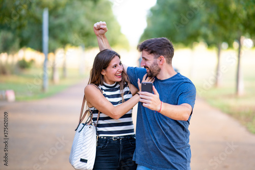Happy couple surprised to receive an acceptance notification on their smartphone in the park