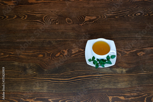 White tea pair with herbal tea stands on a wooden table. View from above. Fresh green leaves and sprigs of mint lie on a saucer. Wood texture. Place for your text.