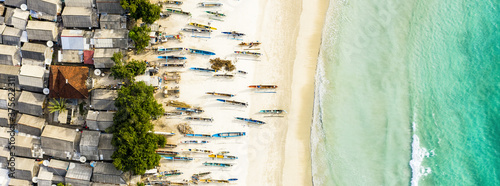 Stunning aerial view of a fishing village with houses and boats on a white sand beach bathed by a beautiful turquoise sea. Tanjung Aan Beach, east of Kuta Lombok, West Nusa Tenggara, Indonesia. photo