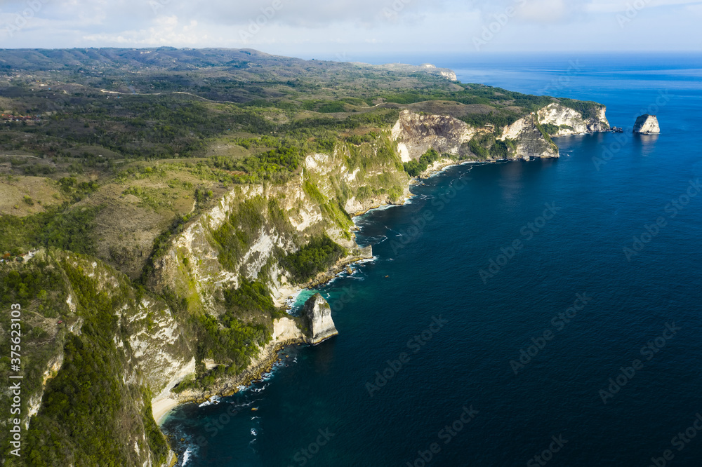 View from above, stunning aerial view of a green limestone cliff bathed by a turquoise sea during sunset. Nusa Penida, Indonesia. Nusa Penida is an island southeast of Bali, Indonesia. View from above, stunning aerial view of a green limestone cliff bathed by a turquoise sea during sunset. Nusa Penida, Indonesia. Nusa Penida is an island southeast of Bali, Indonesia.