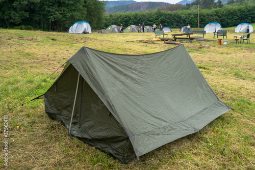Scout camping. Army military tent close up in the base camp. Lots of  tents stand on a field against a green forest.  © GenоМ.