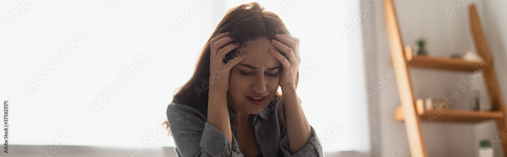 panoramic crop of brunette woman with closed eyes suffering from pain and touching head at home panoramic crop of brunette woman with closed eyes suffering from pain and touching head at home