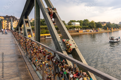 Bridge of lovers with padlocks over the river Main on sunset rays. Lots of metal locks are attached to the railing of the bridge as a sign of eternal love.
