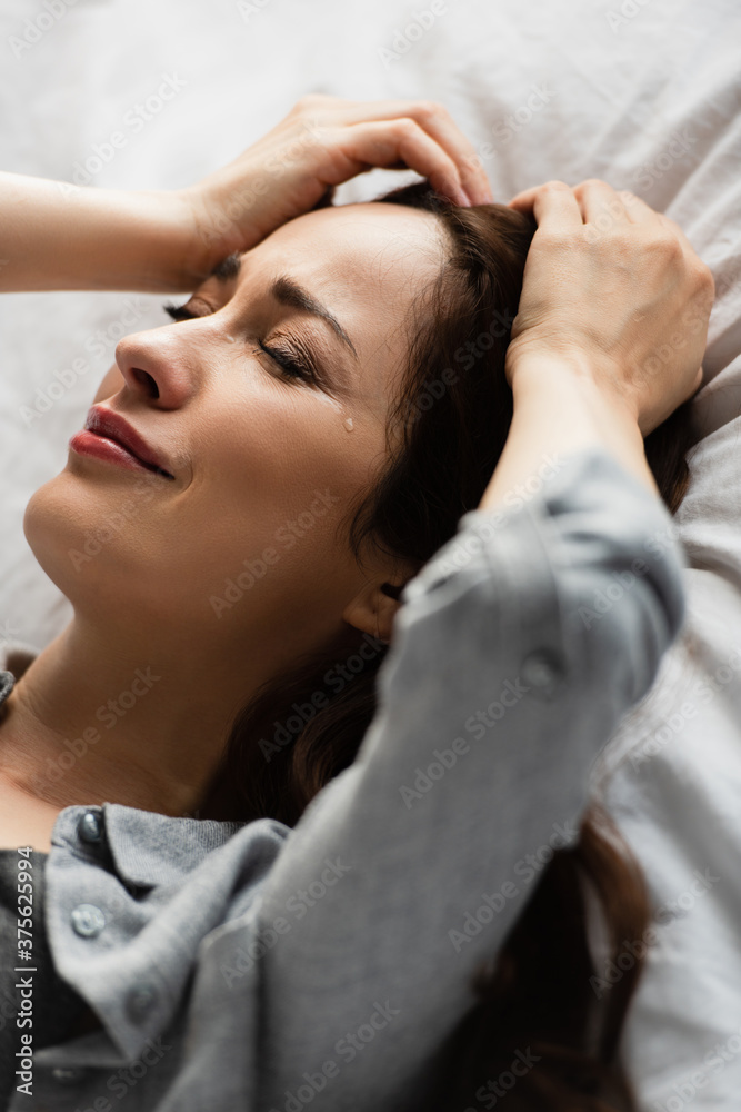 Obraz premium frustrated and brunette woman with closed eyes touching hair while crying on bed