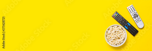 Two remotes from the TV, TV tuner and a bowl of popcorn on a yellow background. Concept series, film, sports. Banner. Flat lay, top view