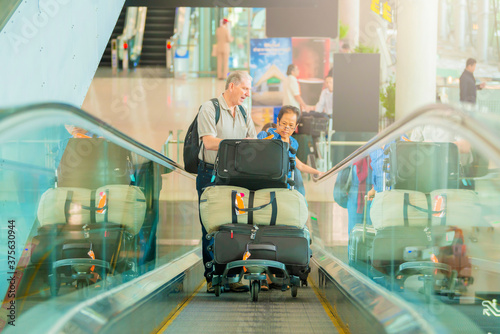 Senior couple walking on escalator while carrying a luggage in the airport hall.