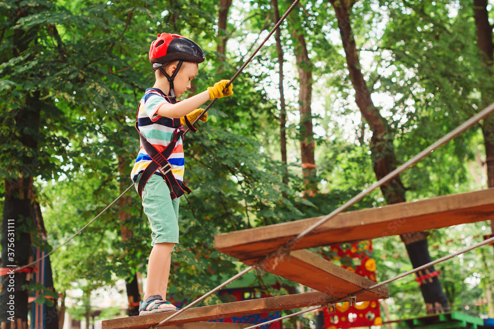 Cute kid climb the rope road. Adventure climbing high wire park. Boy wearing helmet and safety equipment.