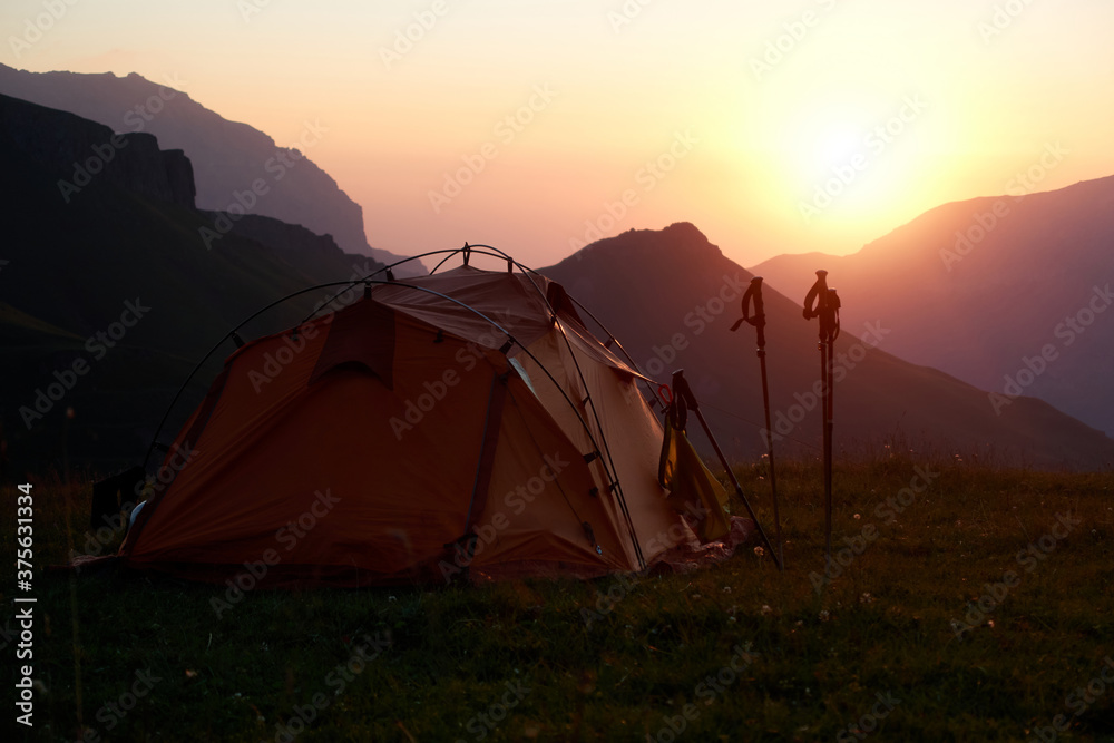 Tourist tent and trekking poles on the background of mountains at sunrise. Dawn in the mountains. Tourist camp in the mountains.