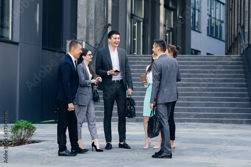 Male and Female Business People Discuss Business. Group of six young caucasian business people men and women meeting discussing outside office building