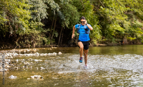 Young man in sports equipment running in mountain river 