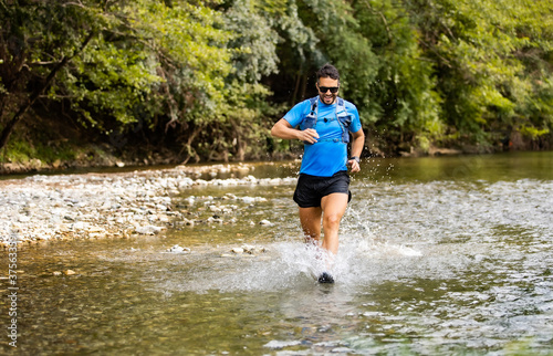 Young man in sports equipment running in mountain river 