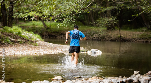 Young man in sports equipment running in mountain river 