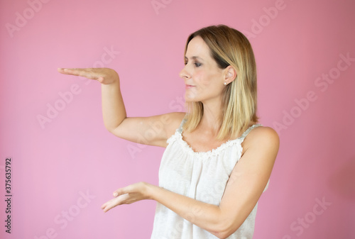 Beautiful woman pointing something on pink background © Danko