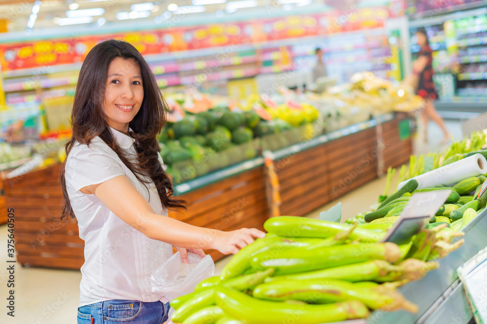 Asian woman in the supermarket. Asian woman shopping in a supermarket and buying fresh organic vegetables. The concept of healthy eating.