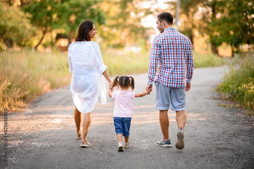 rear view of happy family couple who walks with child holding her hands at sunny summer day rear view of happy family couple who walks with child holding her hands at sunny summer day