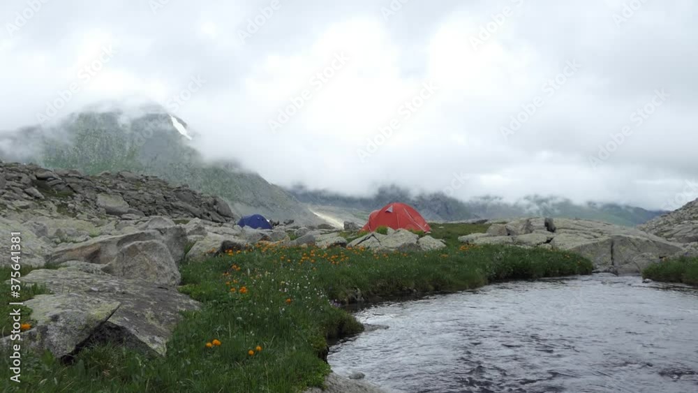 Adventures in nature. Clean water. Tent camp. A stream with melted glacial water flows between rocks in the mountains. Siberia, Altai. Adventures in nature. Clean water. Tent camp. A stream with melted glacial water flows between rocks in the mountains. Siberia, Altai.