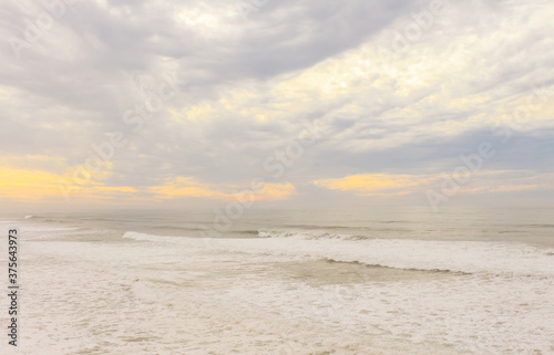 View over sandy beach of Atlantic Ocean with waves crashing and make the splashing water and white air foam bubble at sunset. Natural background.
